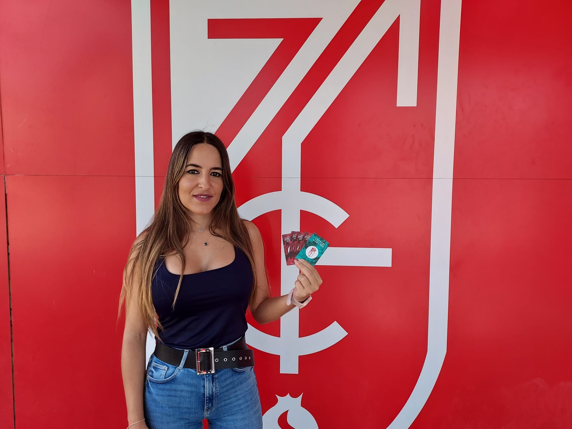 Una joven aficionada posa con varios abonos delante del escudo del Granada (FRAN CALVO)